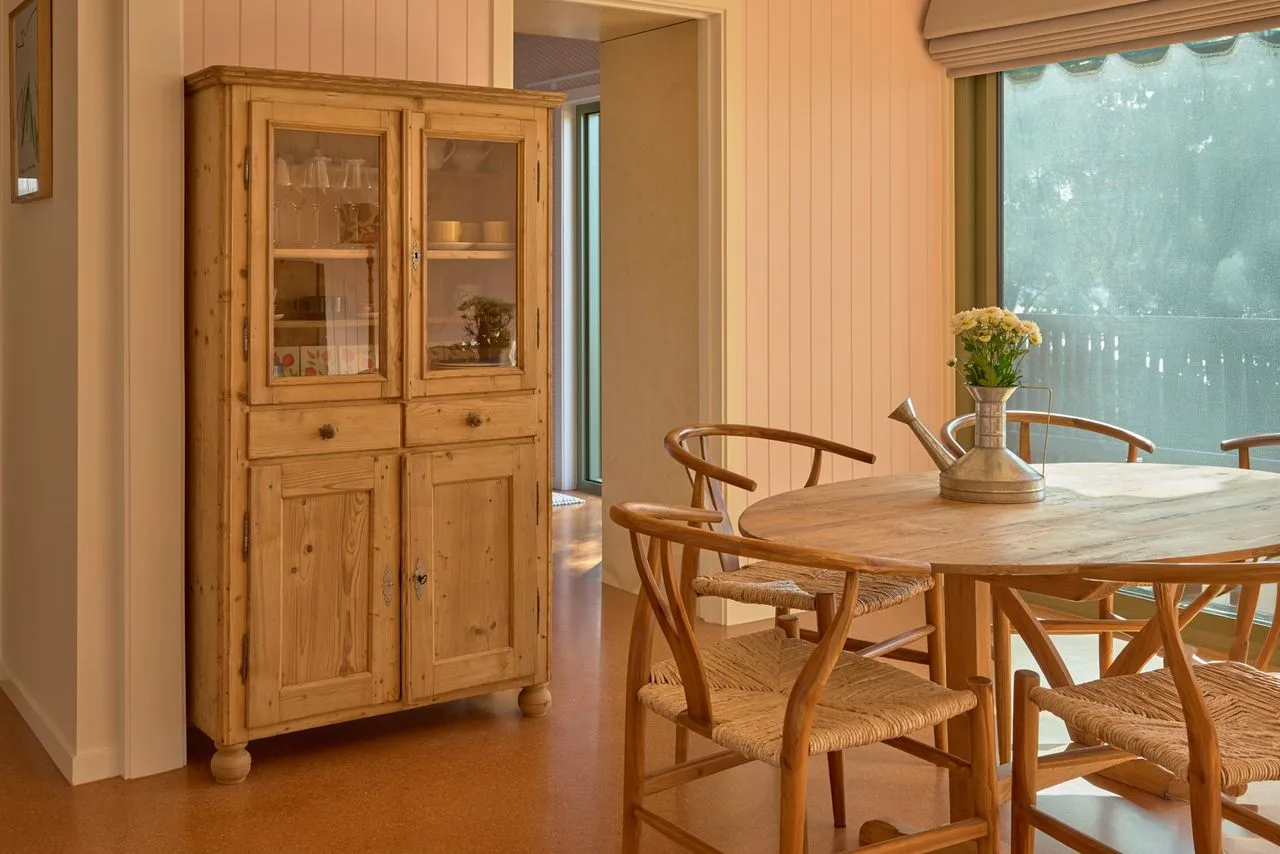 A dining area with a wooden table and chairs beside a large window.