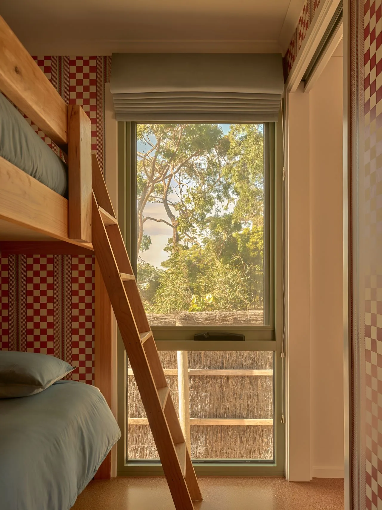 A bunk bed beside a tall window overlooking leafy trees.