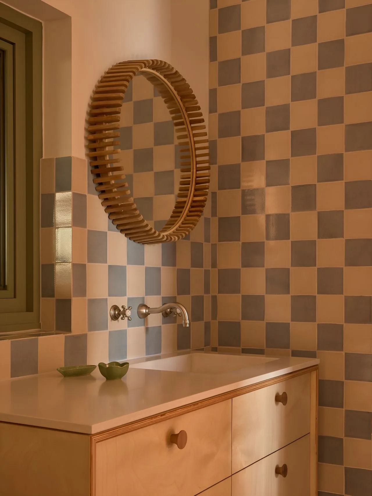 A bathroom vanity with a round mirror against a checkered tile wall.