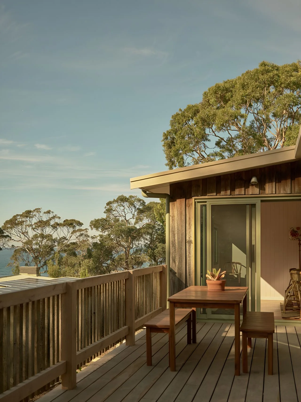 A wooden deck with a dining table overlooks trees and water.