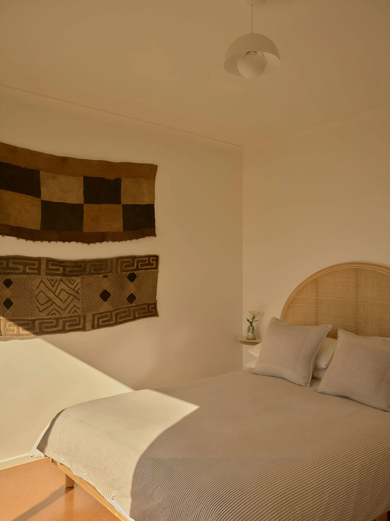 A bedroom with a bed, pillows, and woven wall hangings.