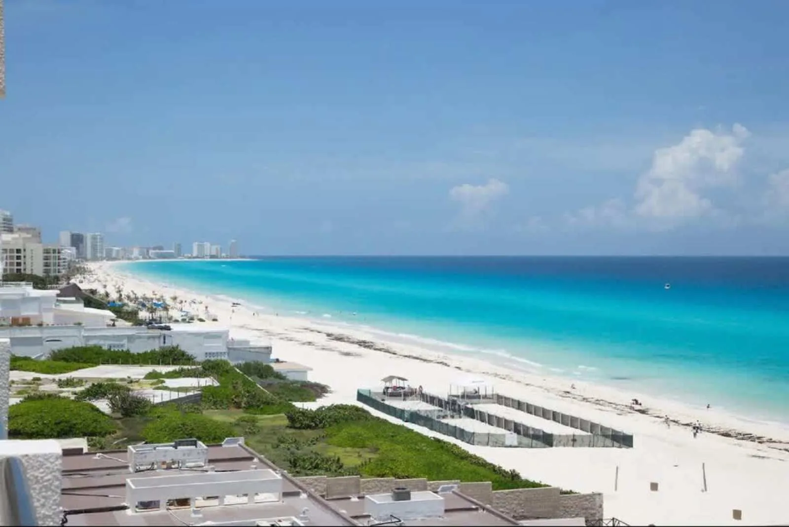A wide sandy beach curves along bright turquoise water beneath a blue sky.