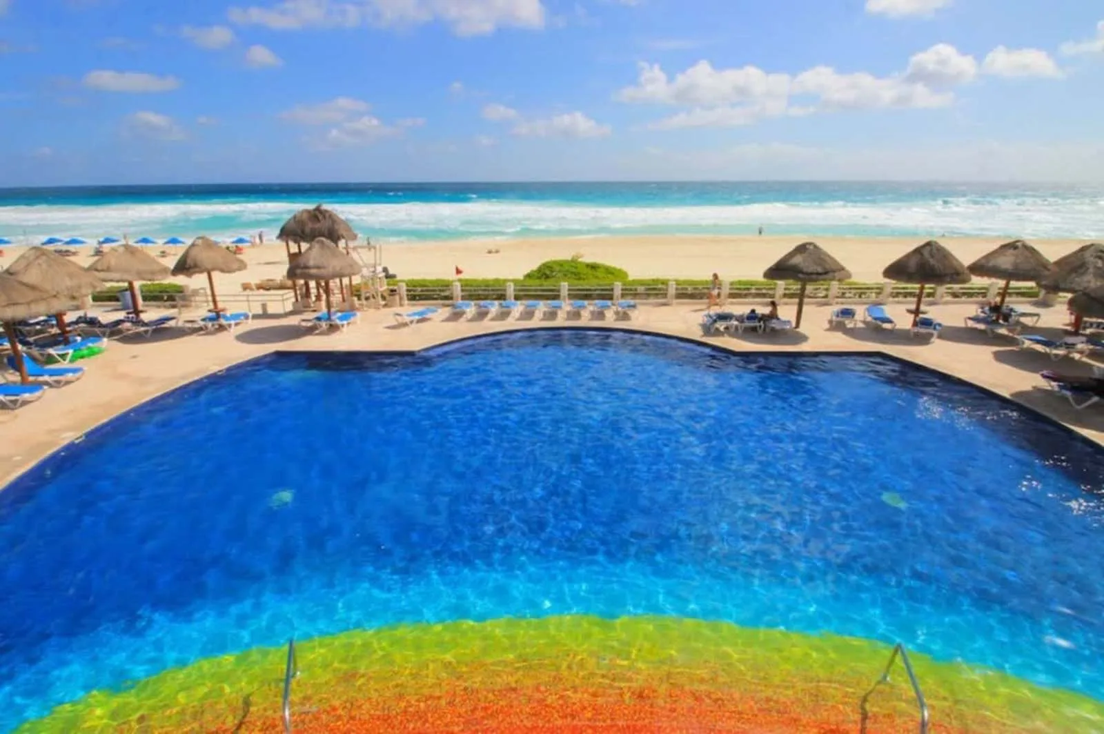 A large swimming pool overlooks a sandy beach and the ocean.