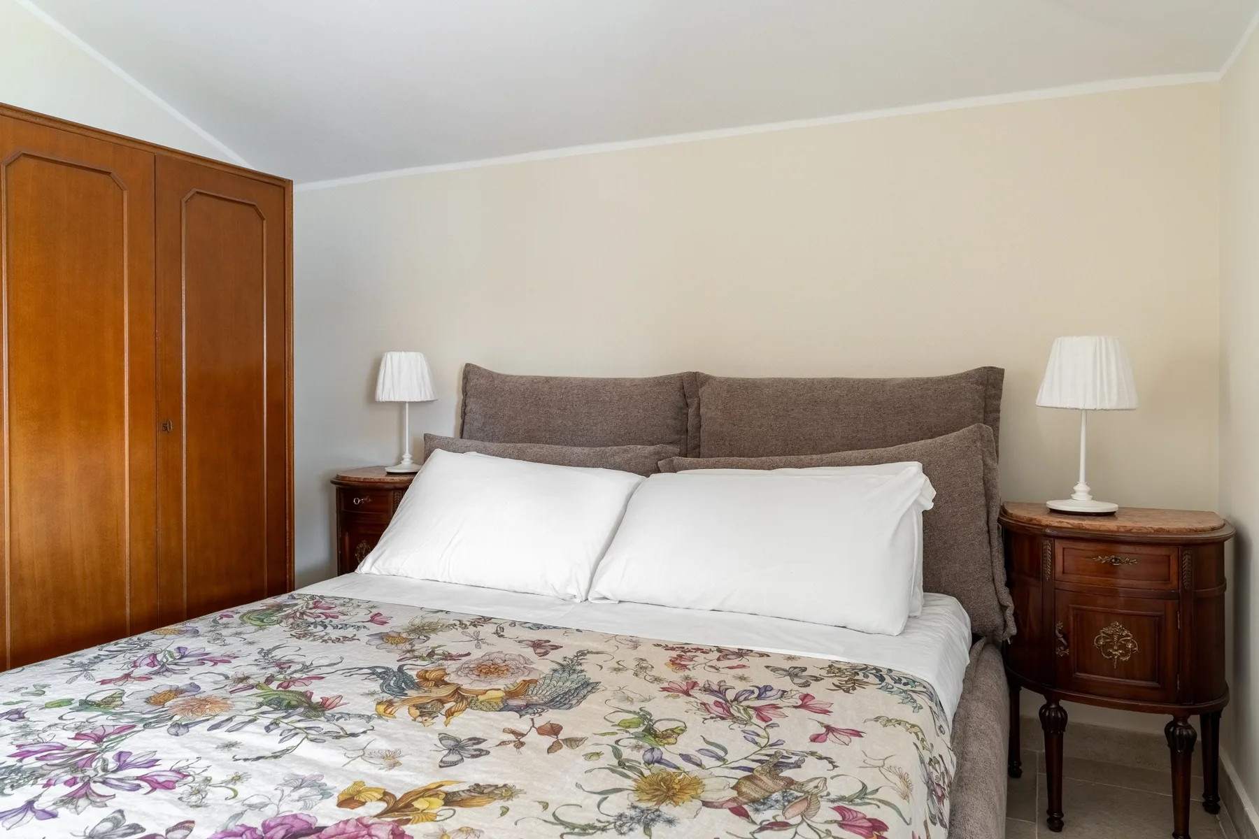 A bedroom with a bed covered in floral bedding and bedside tables.
