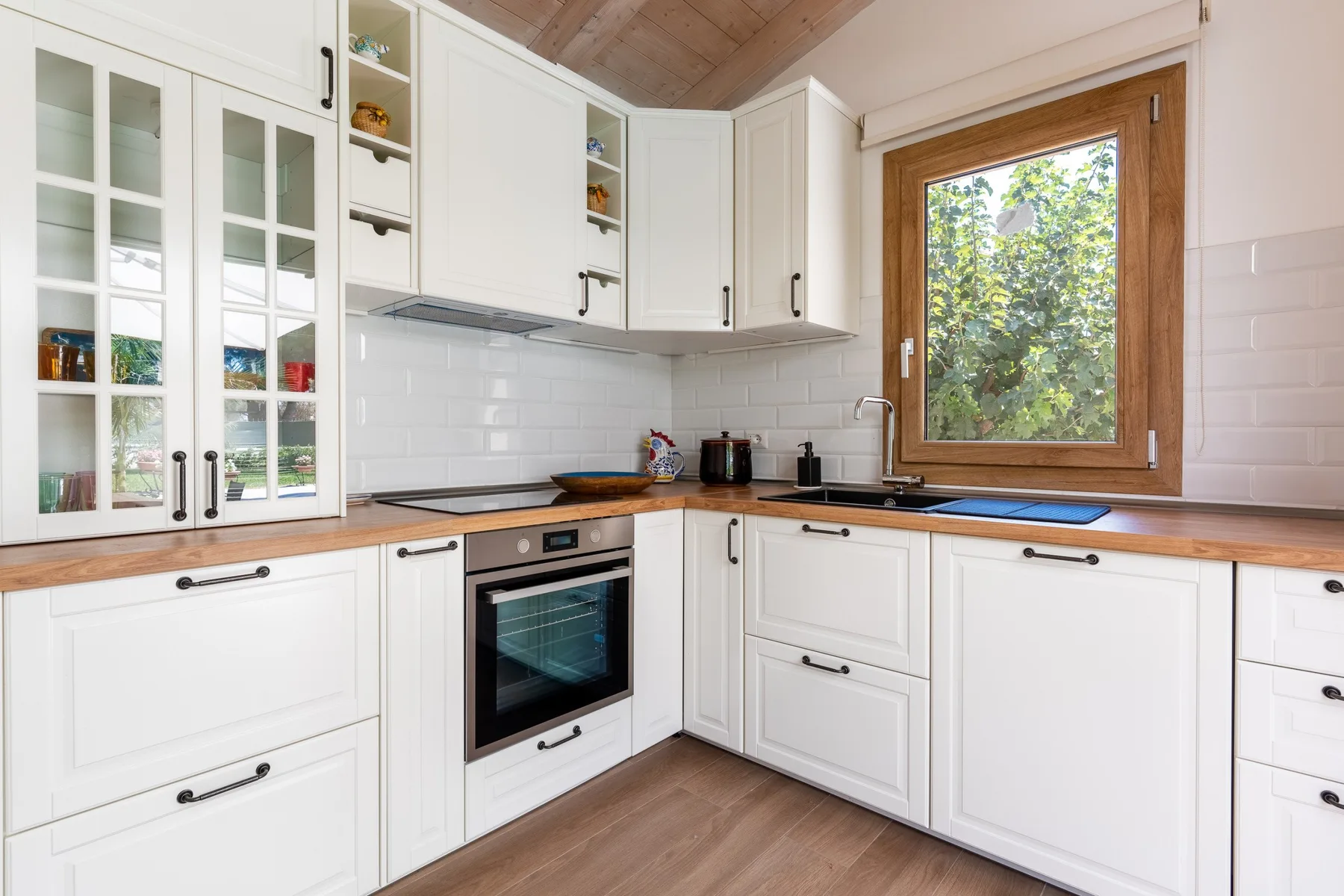 A bright kitchen with white cabinets, a wooden countertop, and a large window.