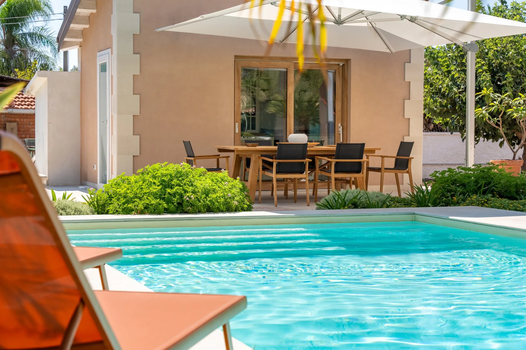 A swimming pool beside a patio dining area and shaded seating.