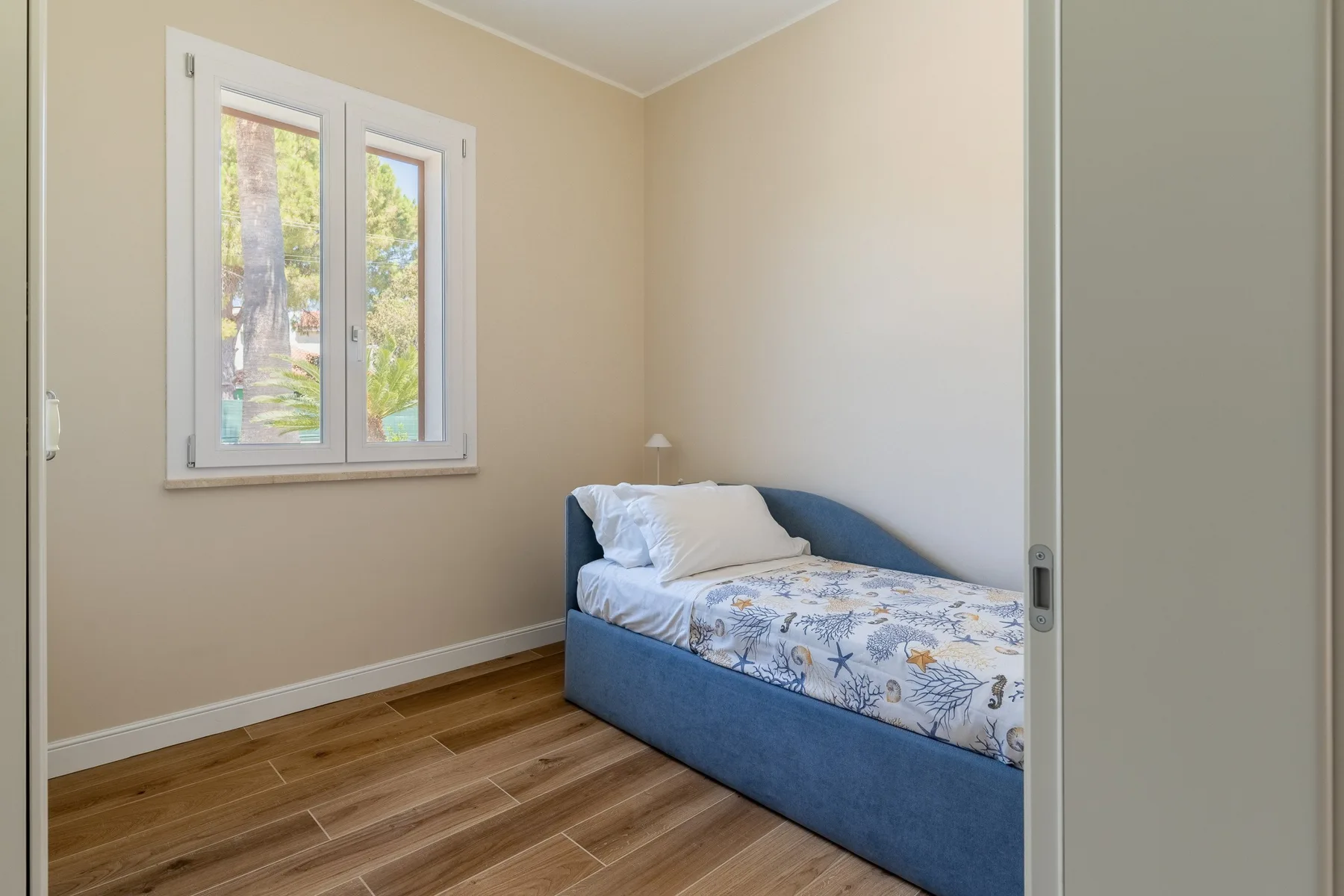 A small bedroom with a blue bed beside a window.