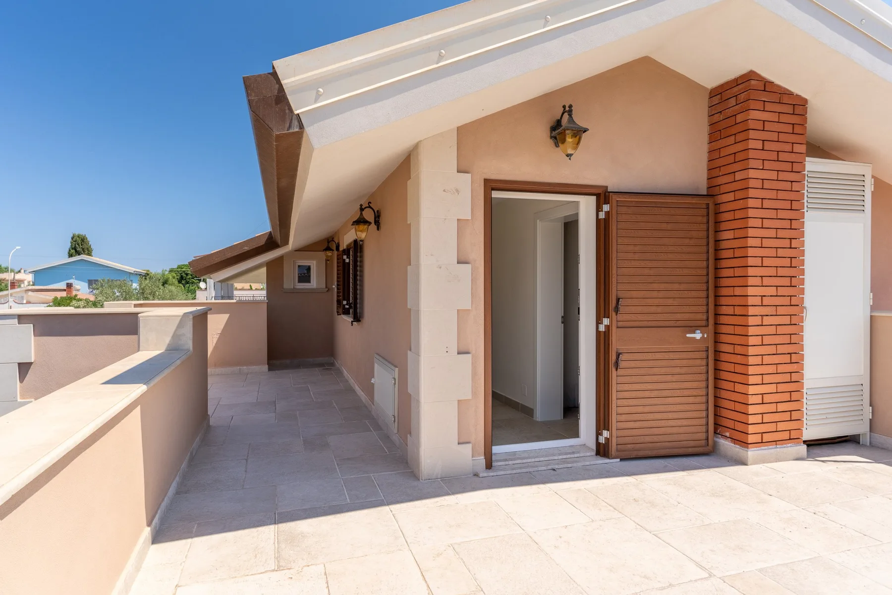 A tiled outdoor terrace leads to an open doorway beside a wooden shutter.