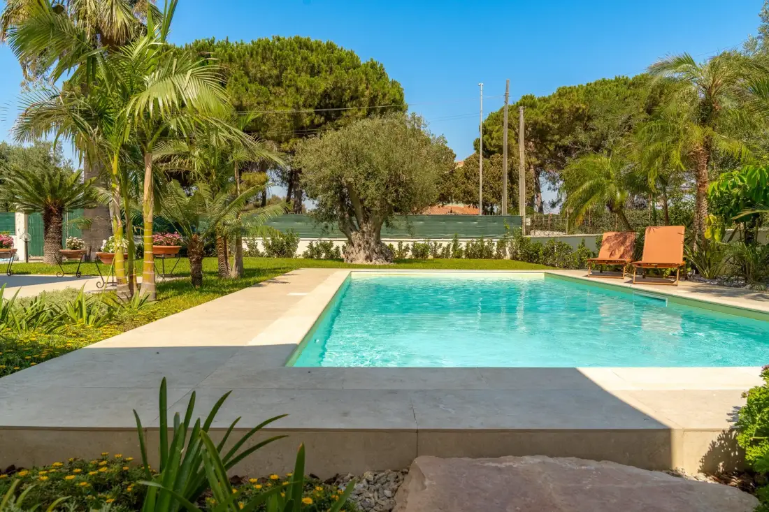 Una piscina al aire libre está rodeada de vegetación y asientos.