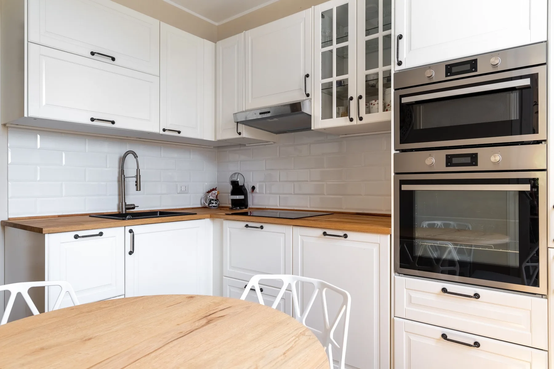 A bright kitchen with white cabinets, wood countertops, and a round dining table.