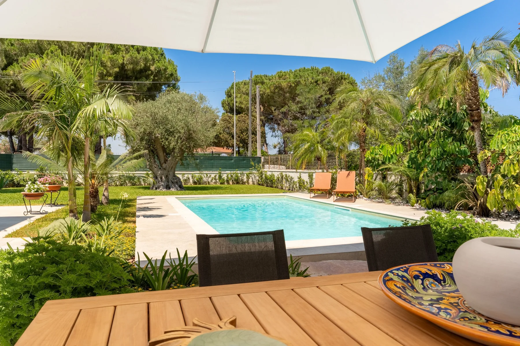 A swimming pool and patio seating are visible among leafy garden plants.