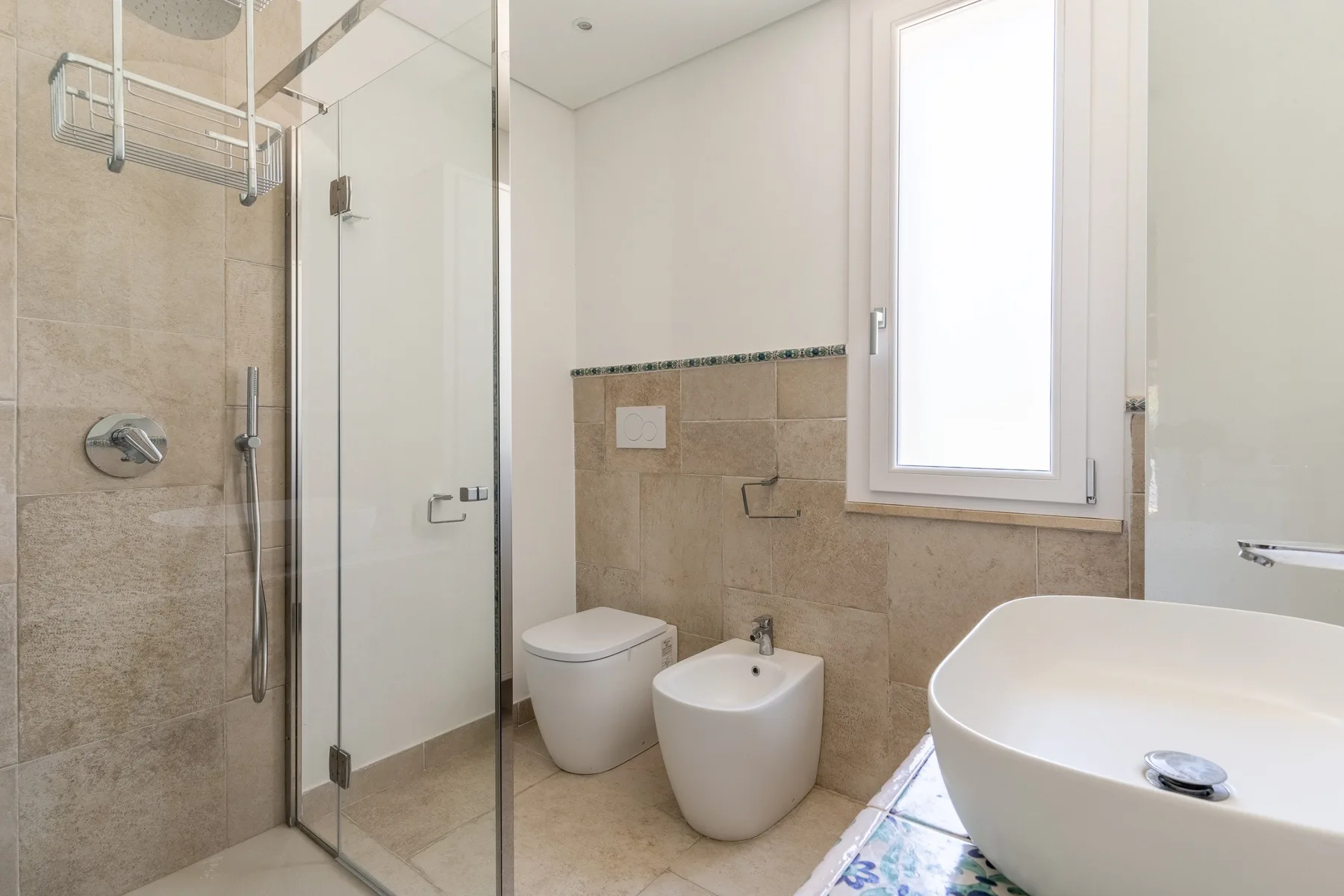 A bright bathroom with a glass shower, toilet, bidet, and freestanding tub.