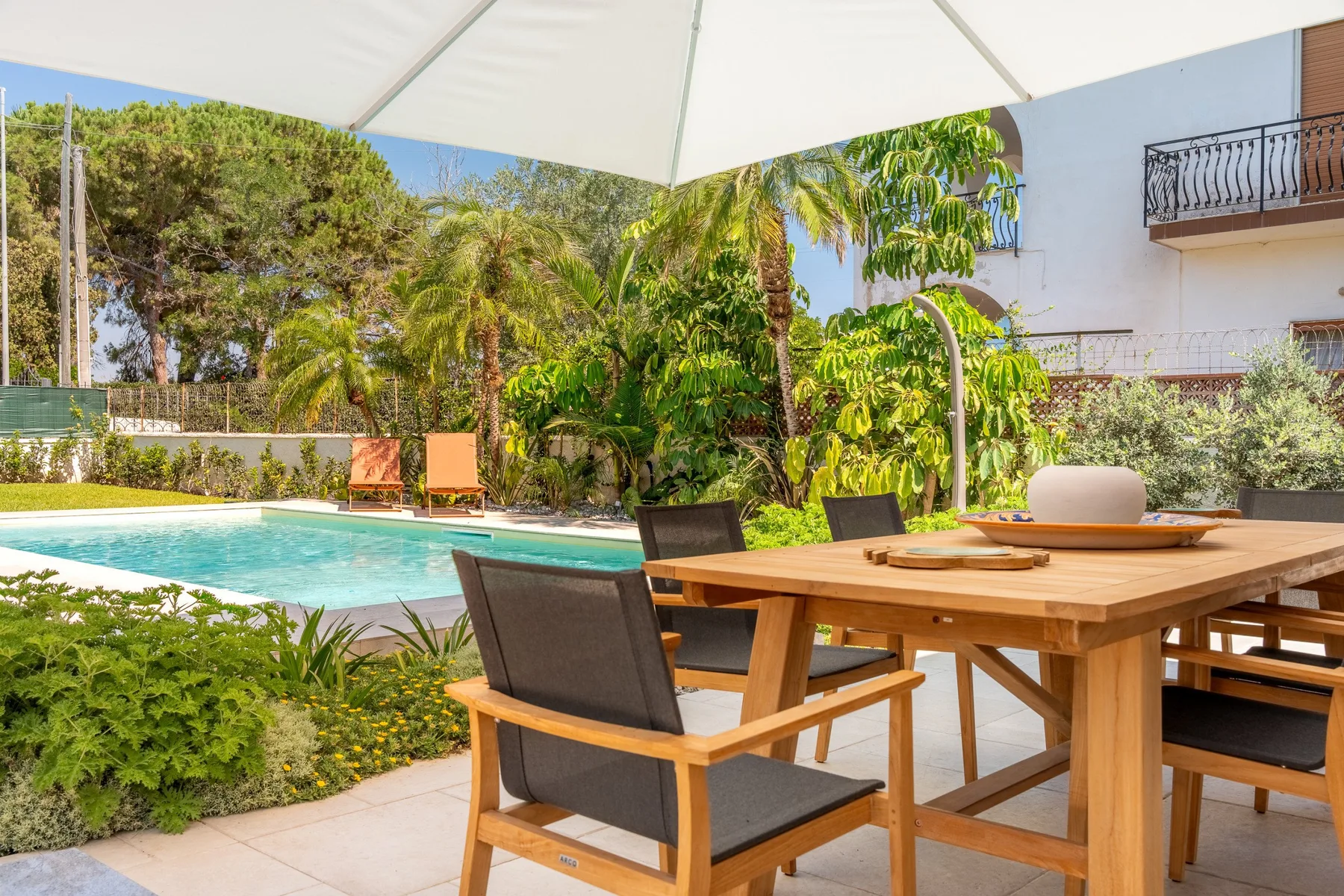 Outdoor dining area beside a swimming pool, with a large shade umbrella overhead.