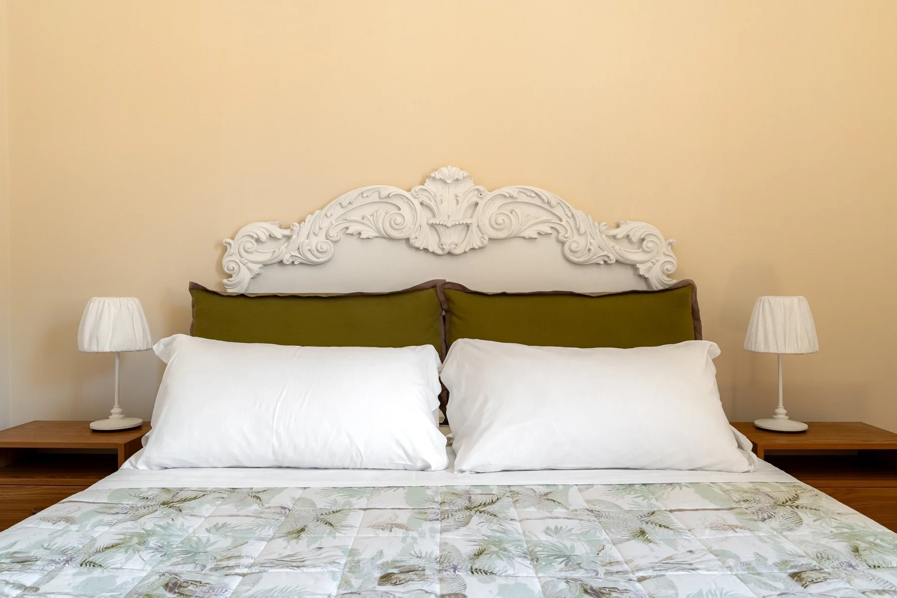 Un dormitorio con una cama tendida, almohadas blancas y lámparas a los lados.