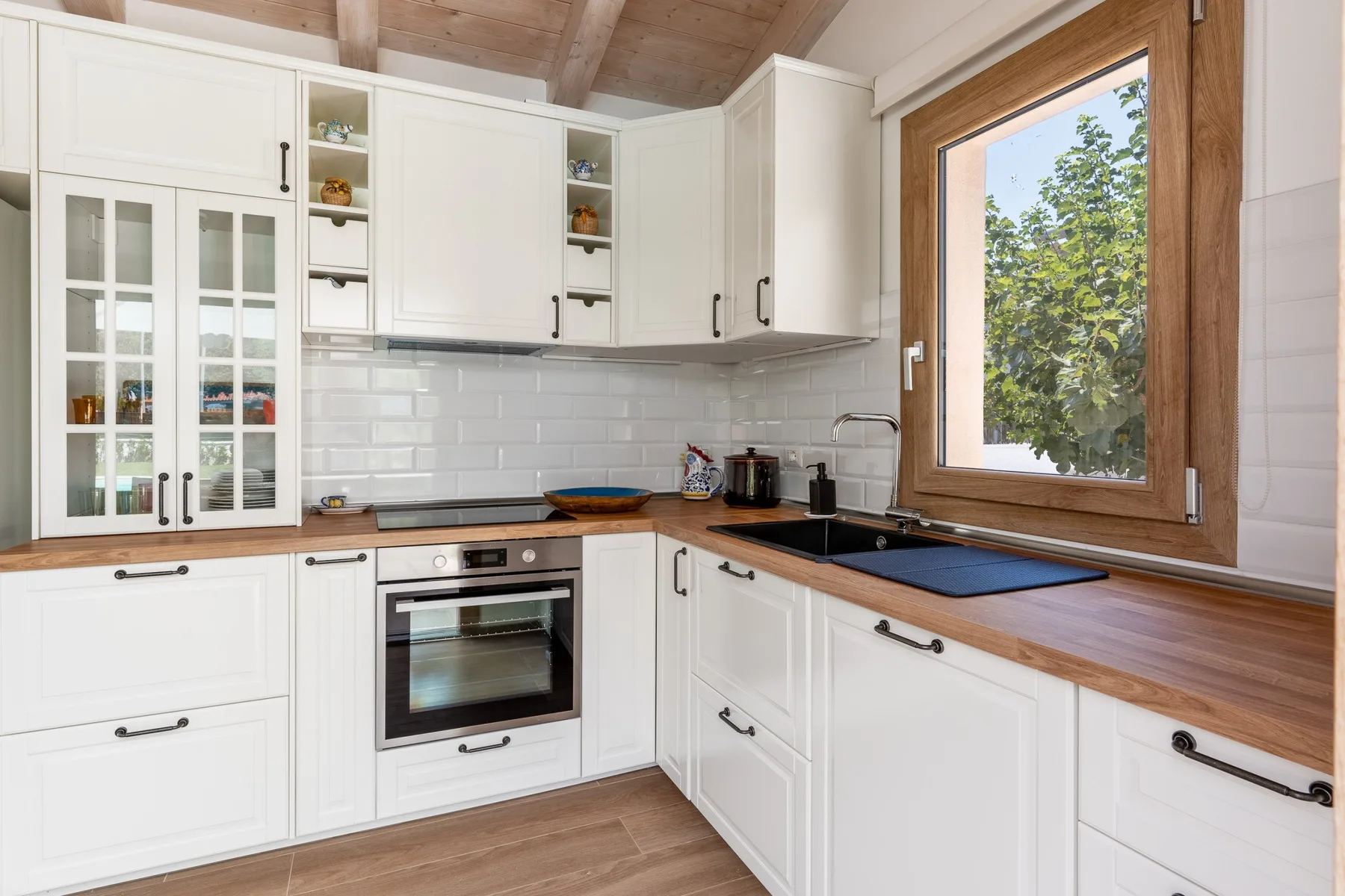 Una cocina luminosa con gabinetes blancos, encimeras de madera y una ventana grande.