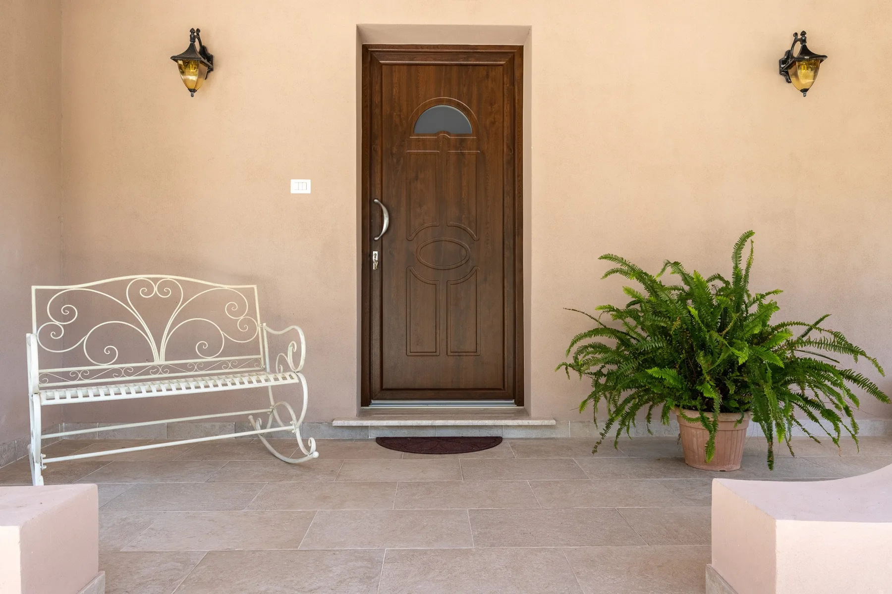 An entryway with a dark wooden door, wall lights, and a potted fern.