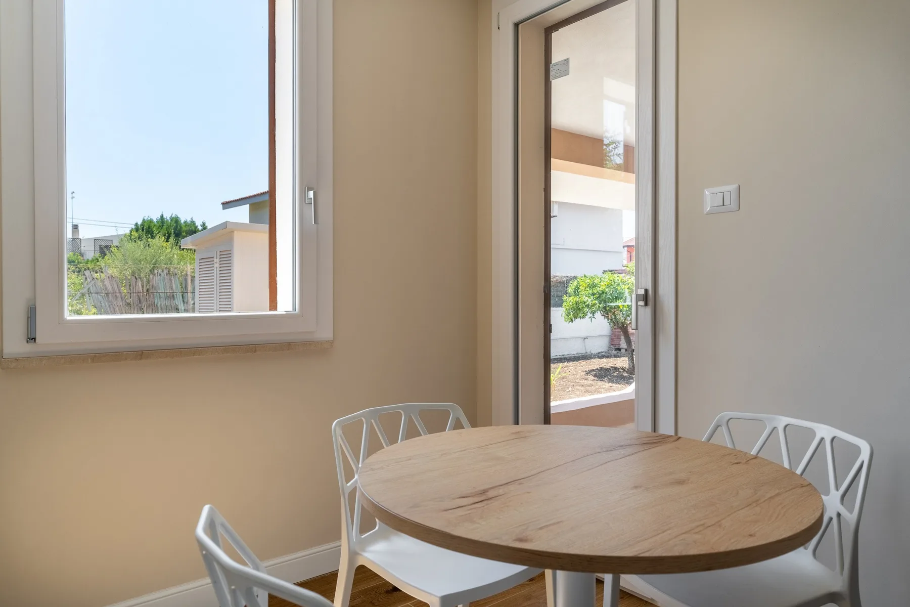 A dining area with a round wooden table and white seating beside a window and glass door.