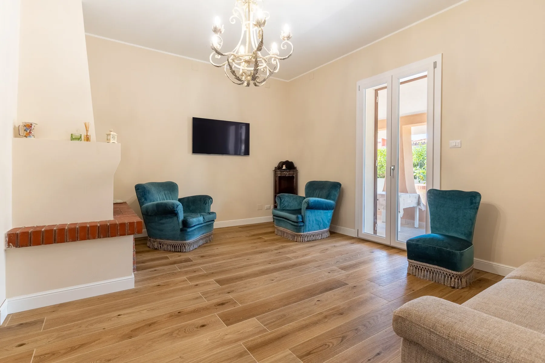 A living room with teal seating, a wall-mounted television, and glass doors.