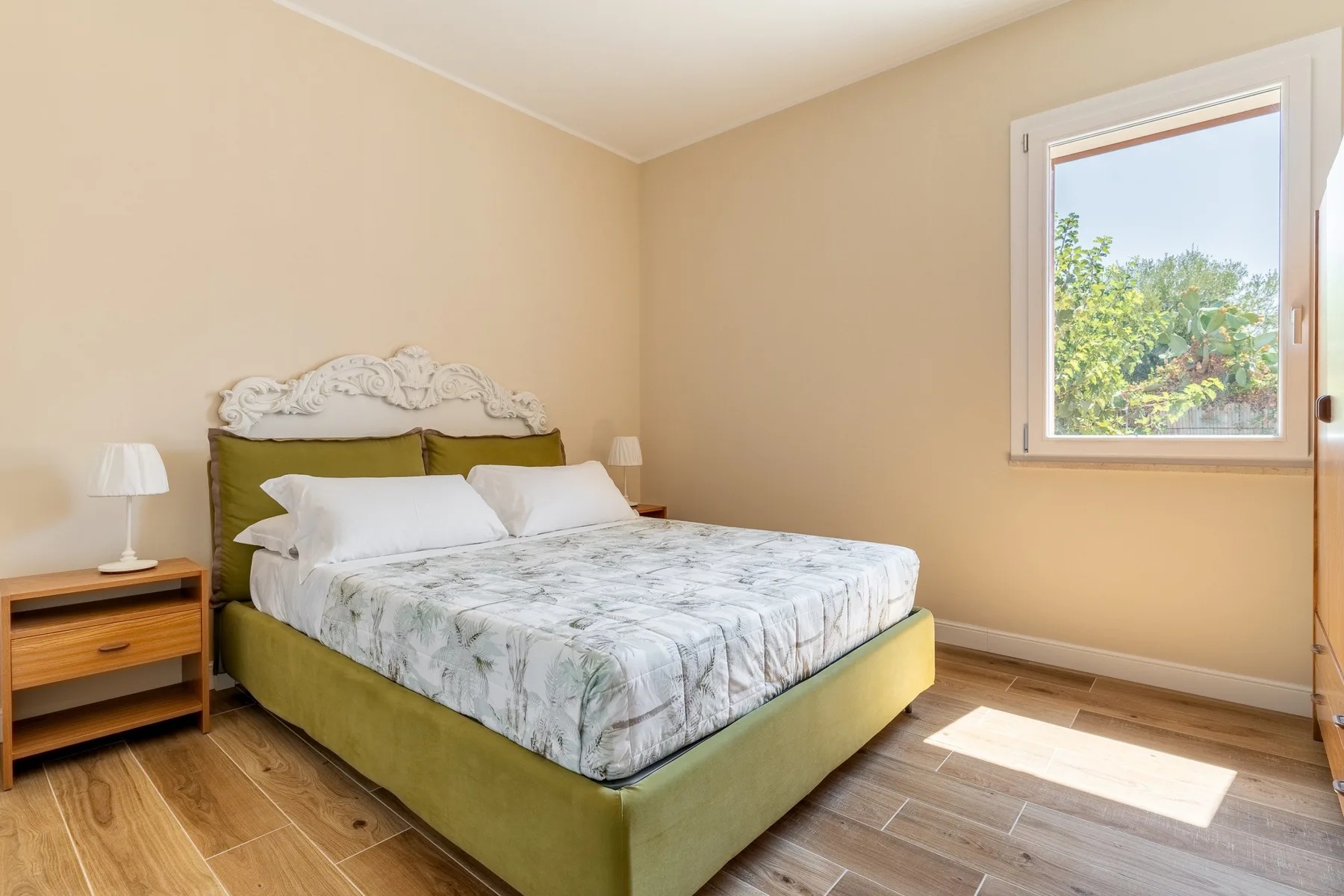 A bedroom with a bed, bedside table, and window overlooking greenery.