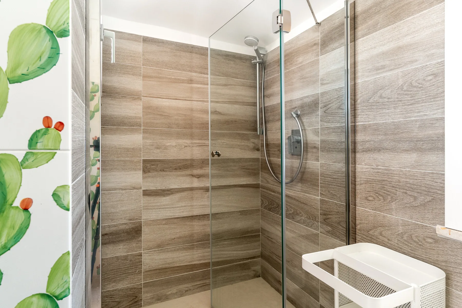 A tiled shower with glass panels and a small white storage unit.