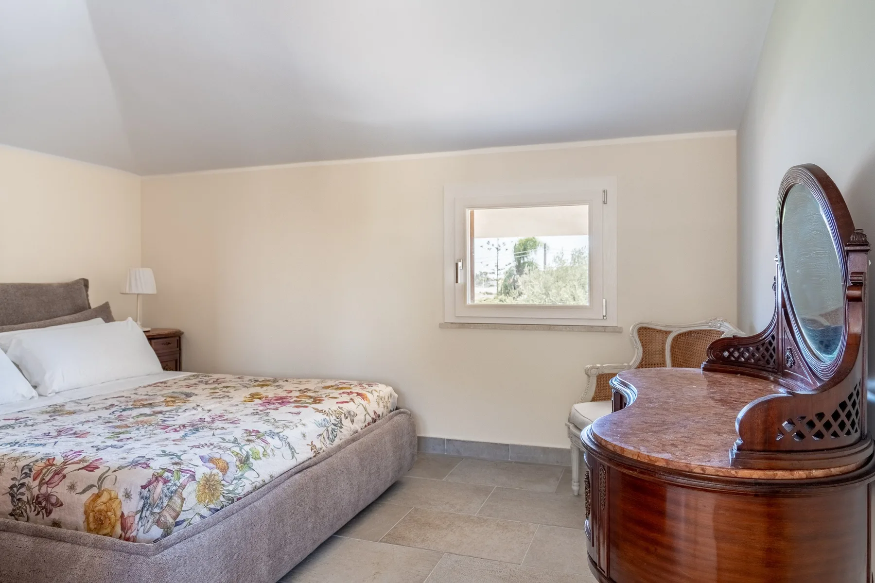 A bedroom with a bed, a window, and a wooden dressing table.