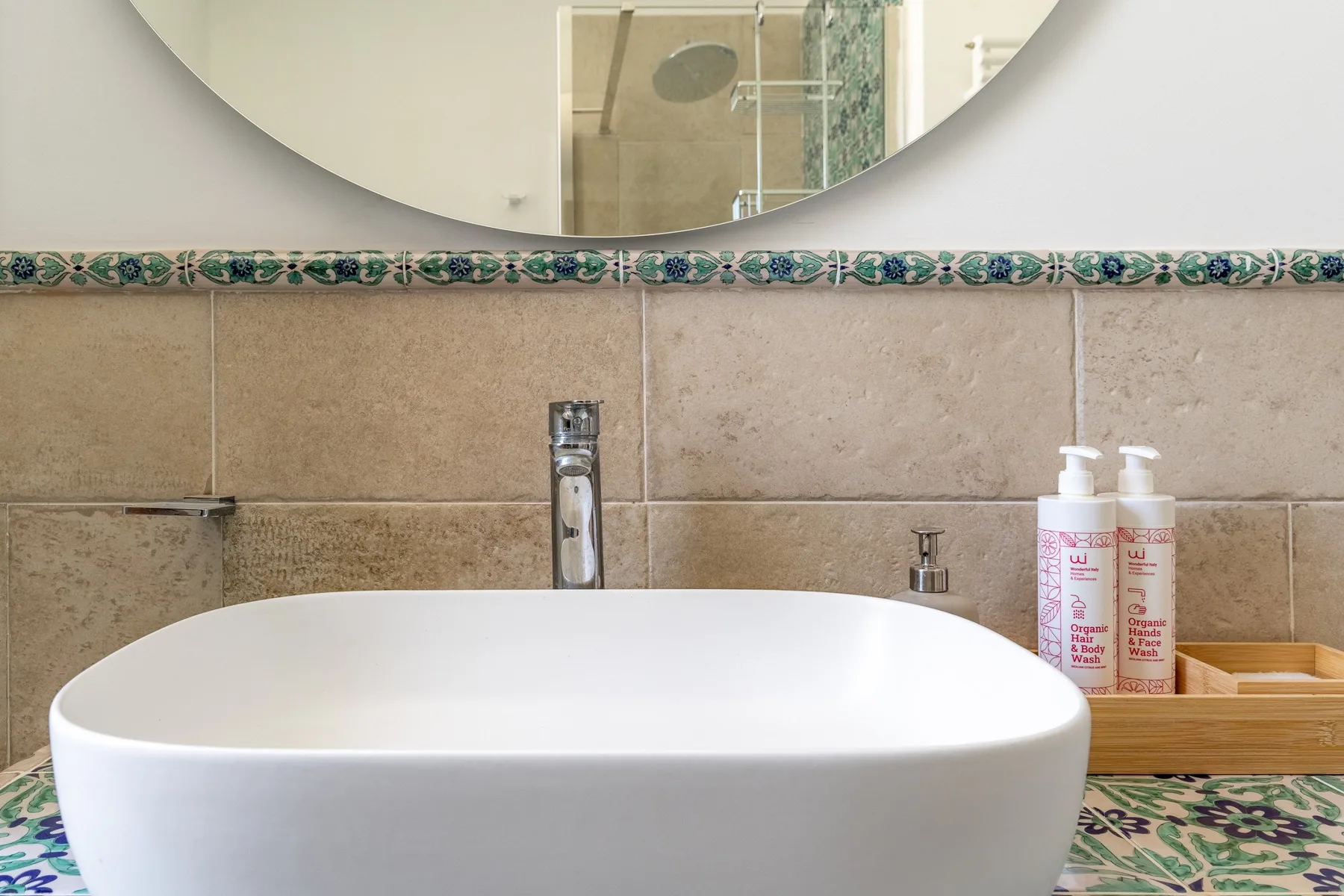 A bathroom vanity with a white basin, tiled backsplash, and round mirror.