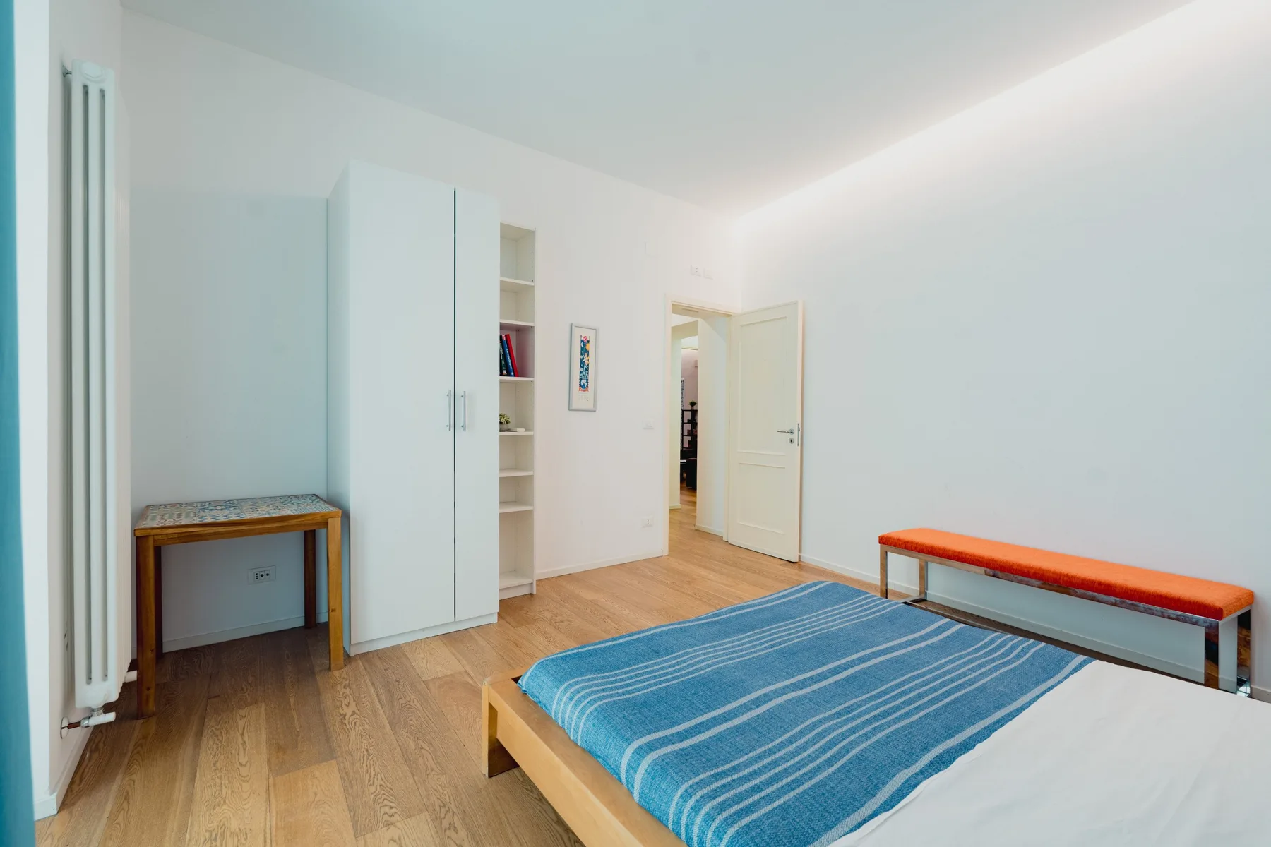 Un dormitorio luminoso con una cama azul, un escritorio y una puerta abierta.