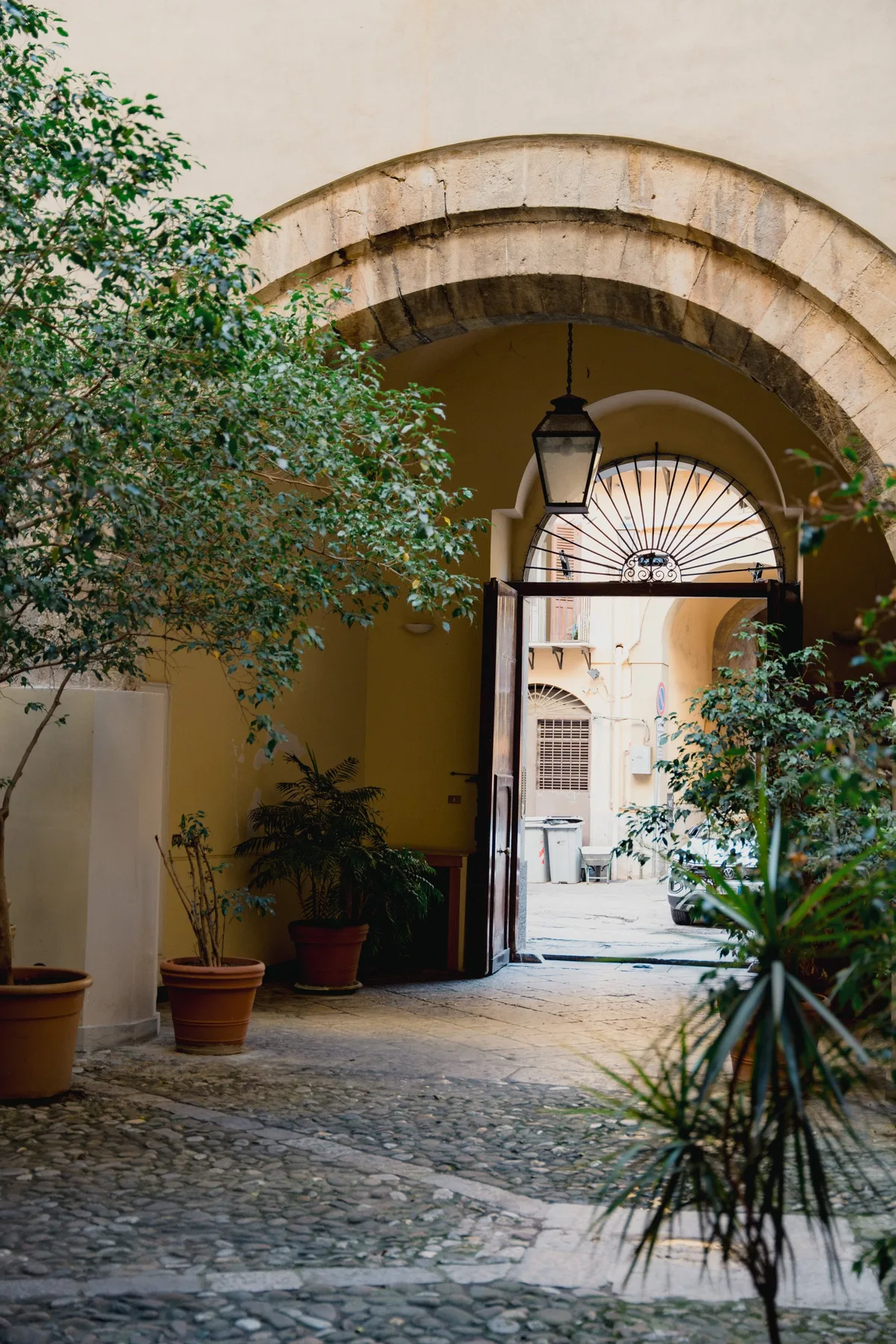 Un pasaje de piedra con arco da a un patio luminoso, con plantas junto al camino.