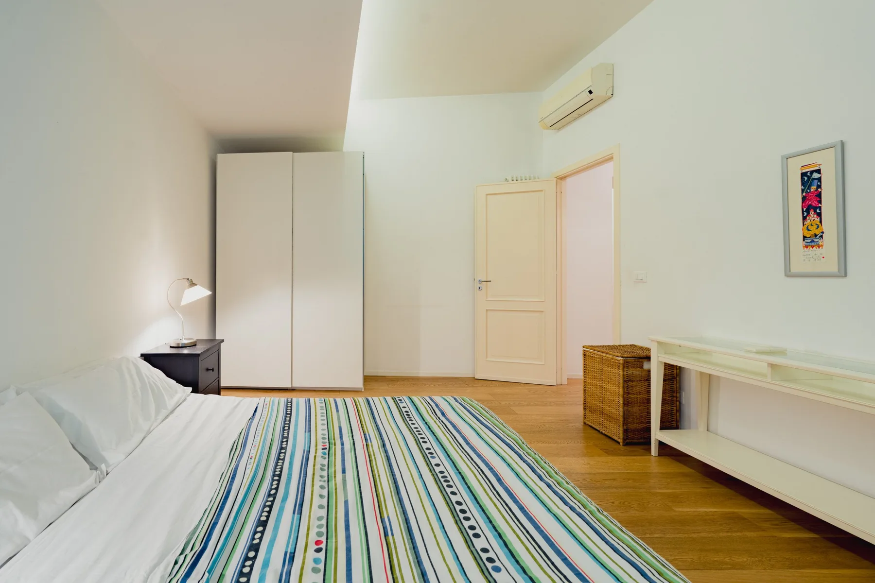 Un dormitorio con una colcha a rayas, un armario y una puerta abierta.