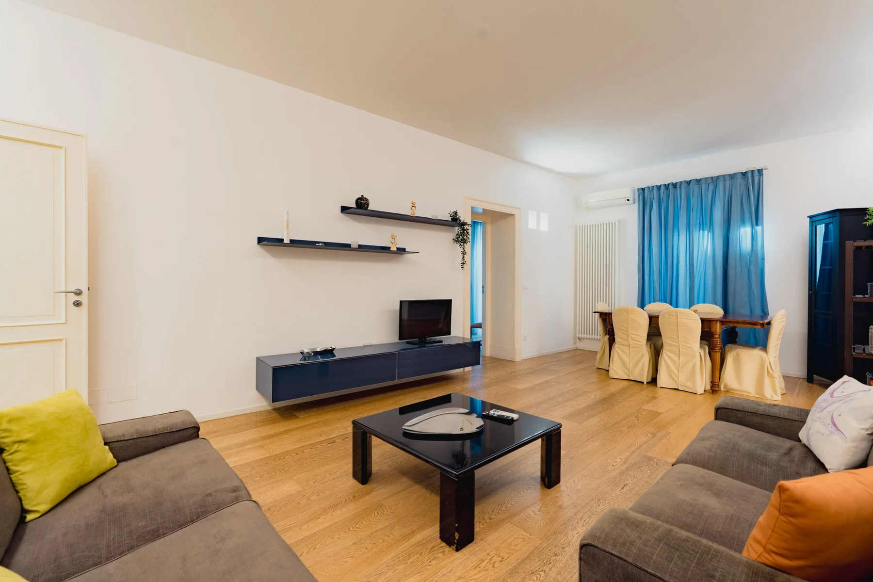 Una sala de estar con asientos, una mesa de centro y un comedor junto a cortinas azules.