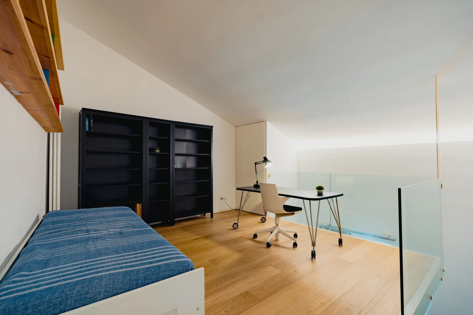 Una zona de trabajo luminosa con escritorio, silla de oficina y cama azul.
