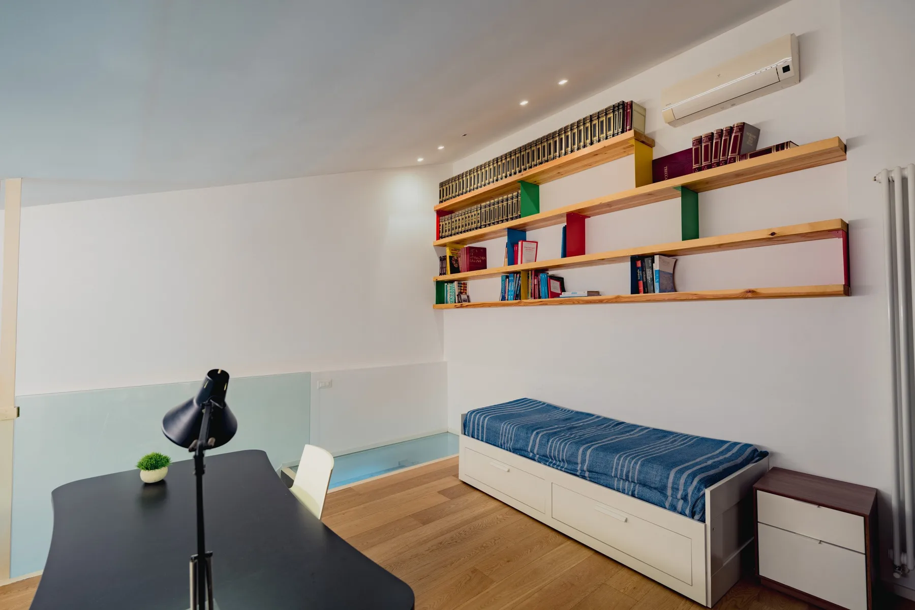 Una luminosa zona de estudio con escritorio, estantes de pared y un diván.