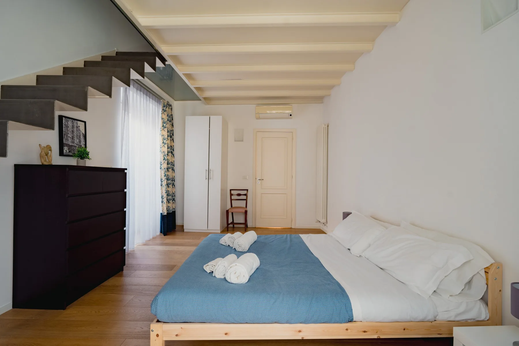 Un dormitorio con una cama cubierta de azul bajo una escalera abierta.