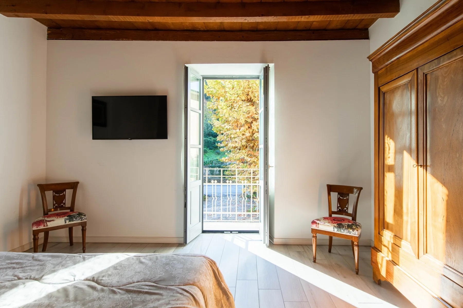 Un dormitorio con una cama, dos sillas y una puerta abierta a un balcón.