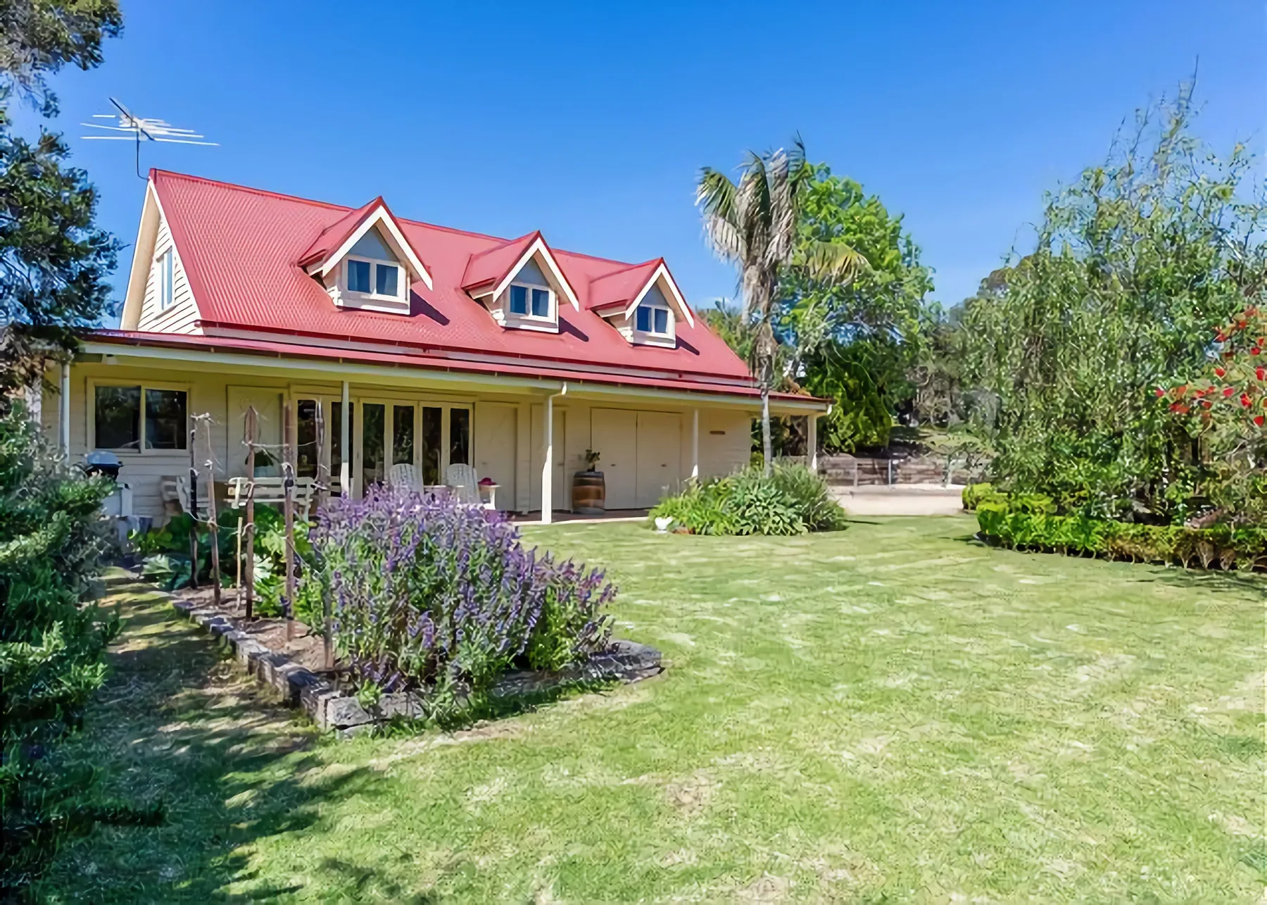 Una casa con techo rojo está junto a un jardín y un césped cuidados.