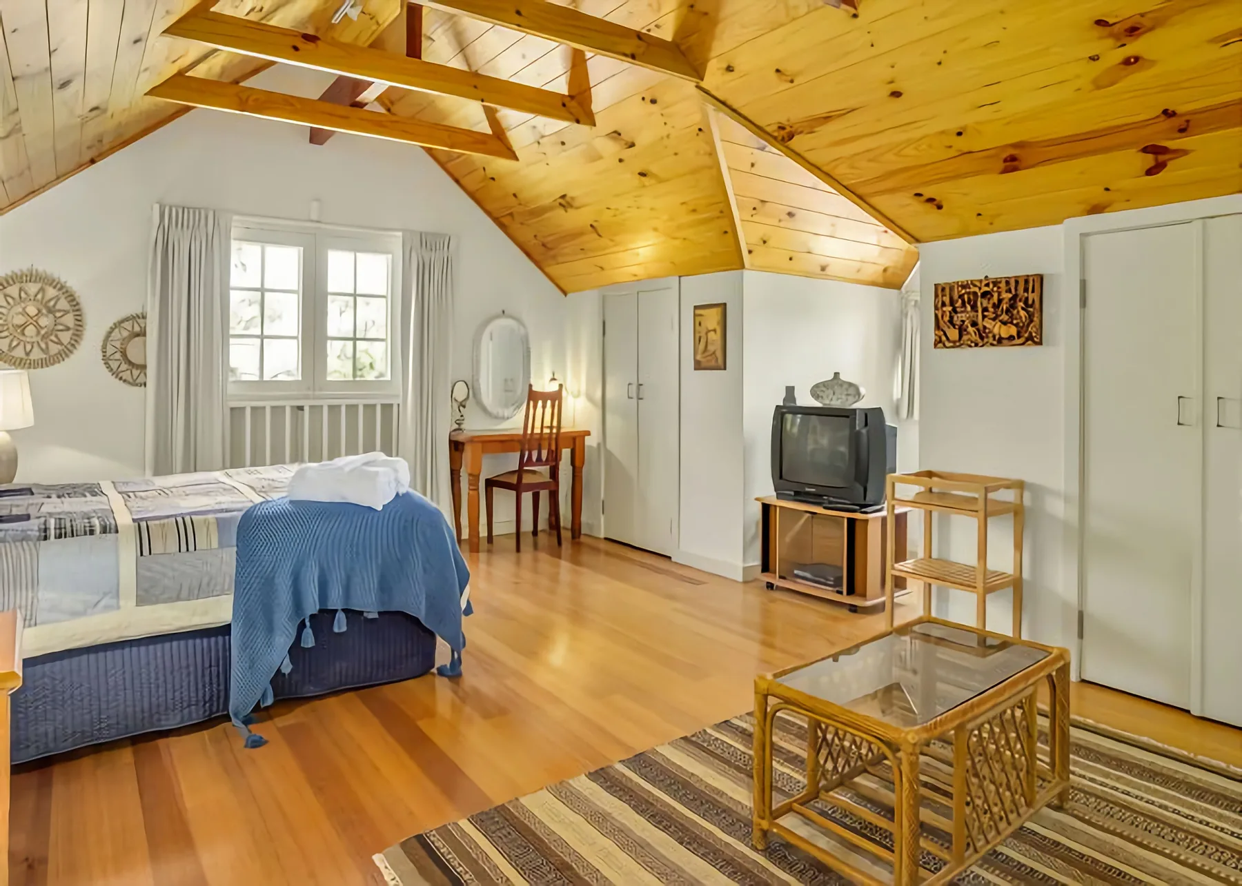 Dormitorio con techo de madera inclinado, cama y zona de estar.