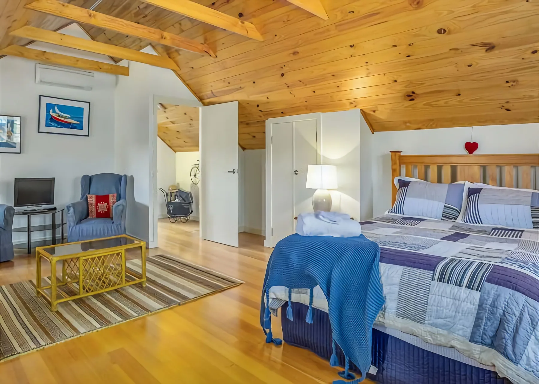 Dormitorio con cama, zona de estar y techo inclinado de madera.