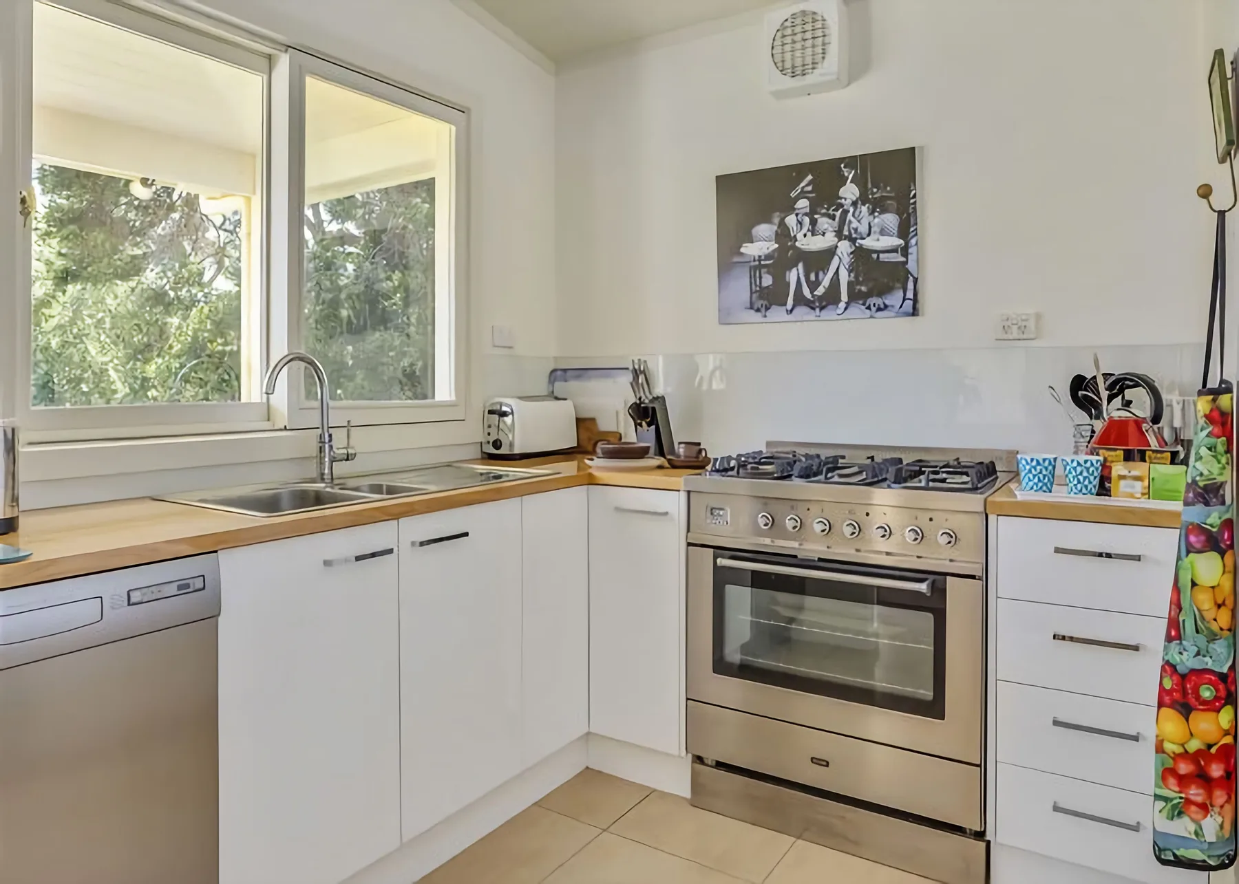 Una cocina luminosa con gabinetes blancos, un fregadero y una estufa de acero inoxidable.