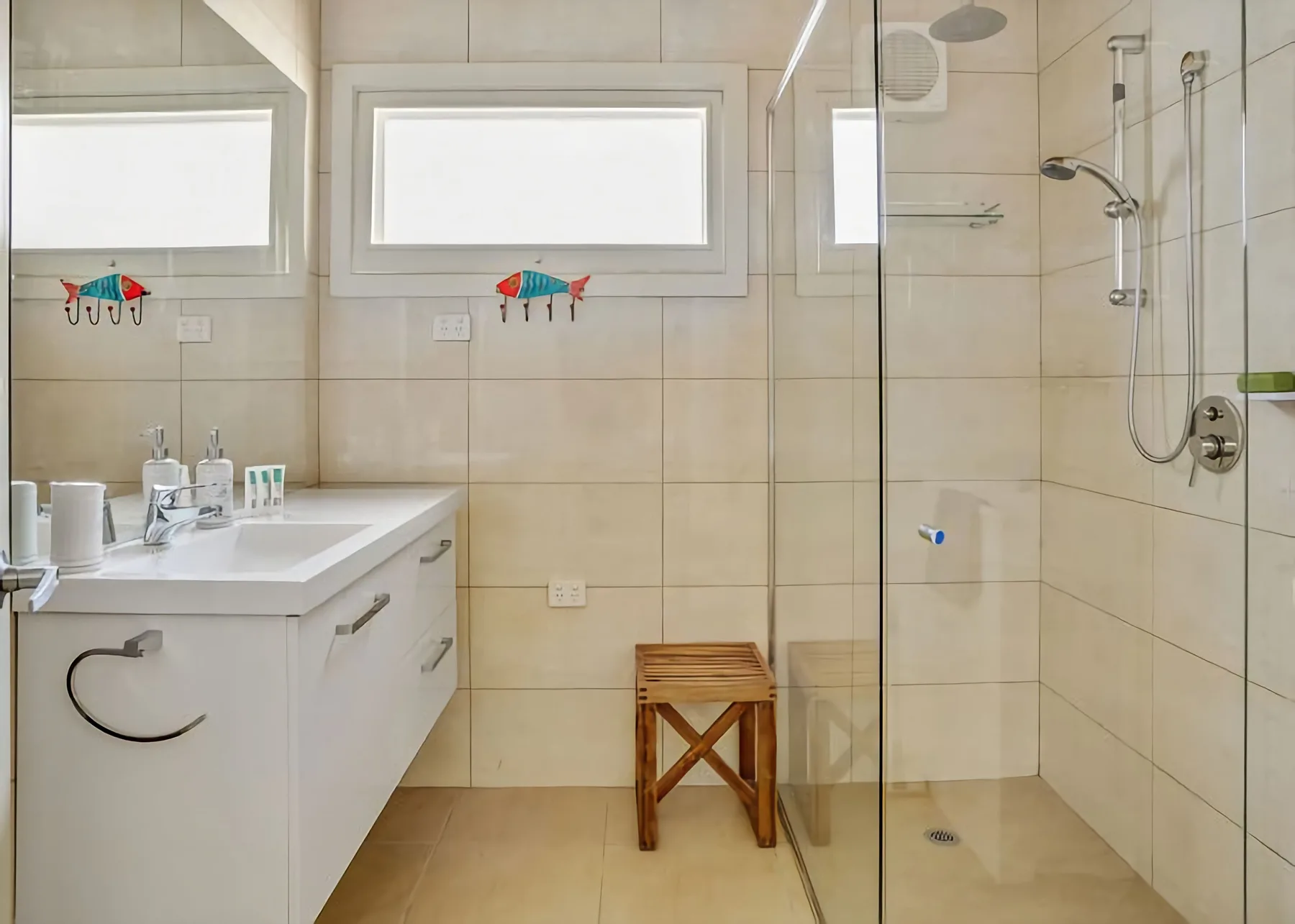 Un baño alicatado con lavabo, dos ventanas y una ducha de vidrio.