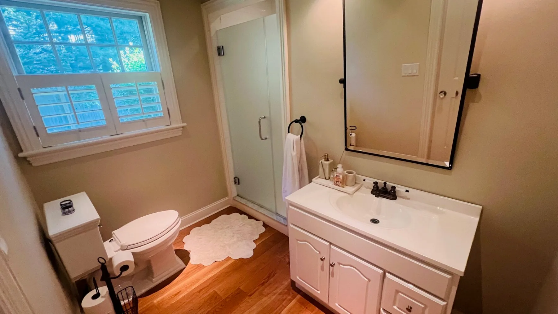 Un baño con tocador blanco, inodoro y ducha junto a una ventana.