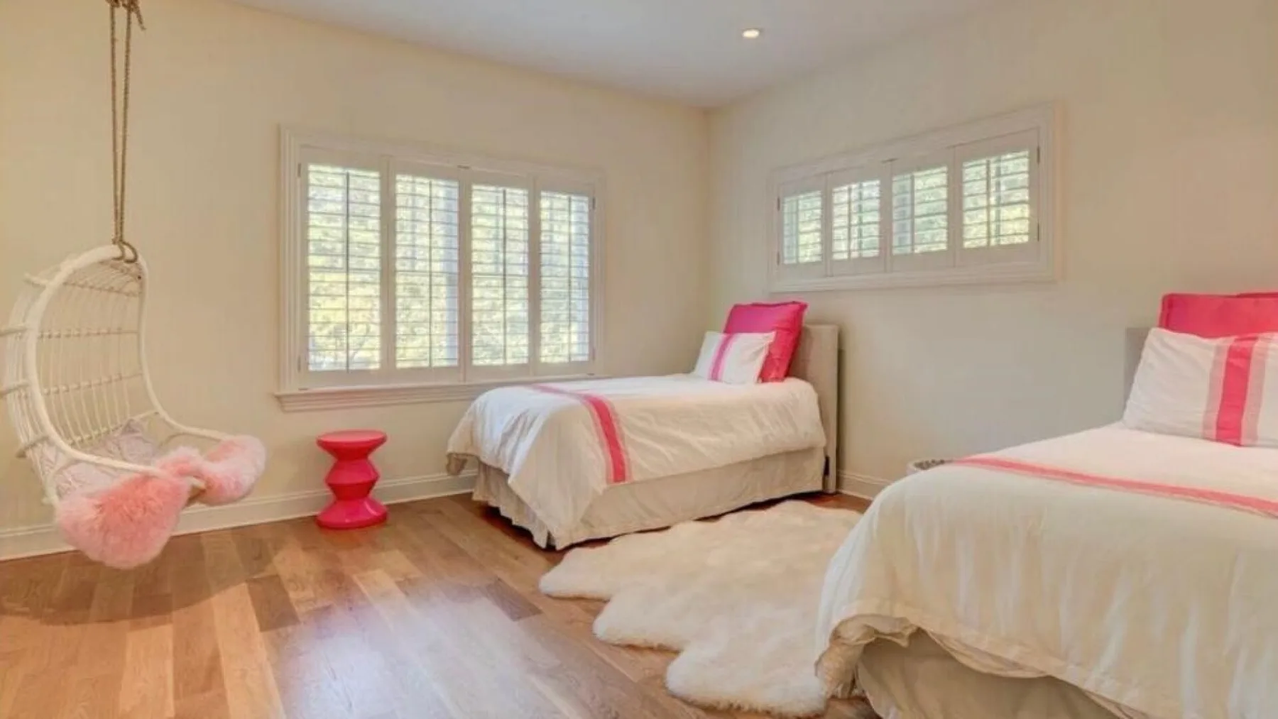 Un dormitorio luminoso con dos camas, ventanas amplias y una silla colgante.