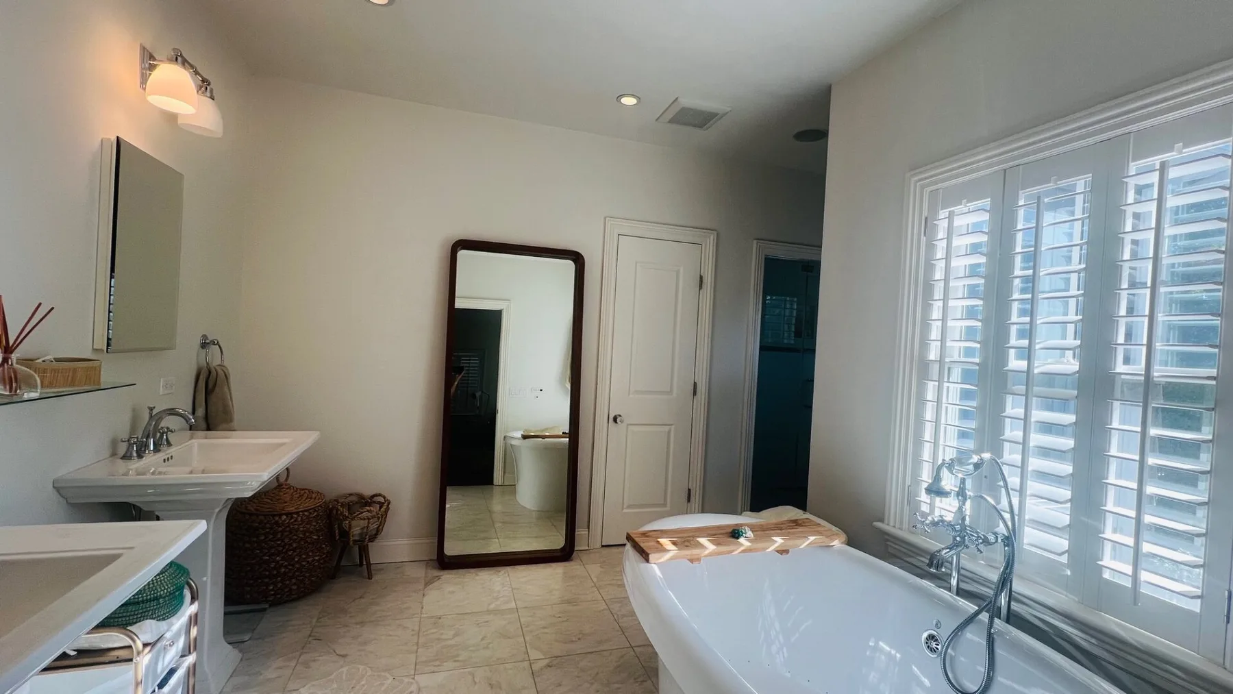 Un baño con bañera, lavabo y grandes ventanas con persianas.