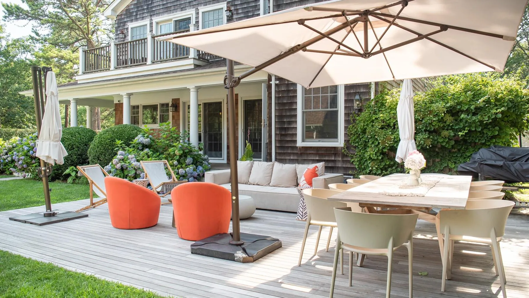 Un patio exterior con asientos, una mesa de comedor y sombrillas grandes junto a una casa.