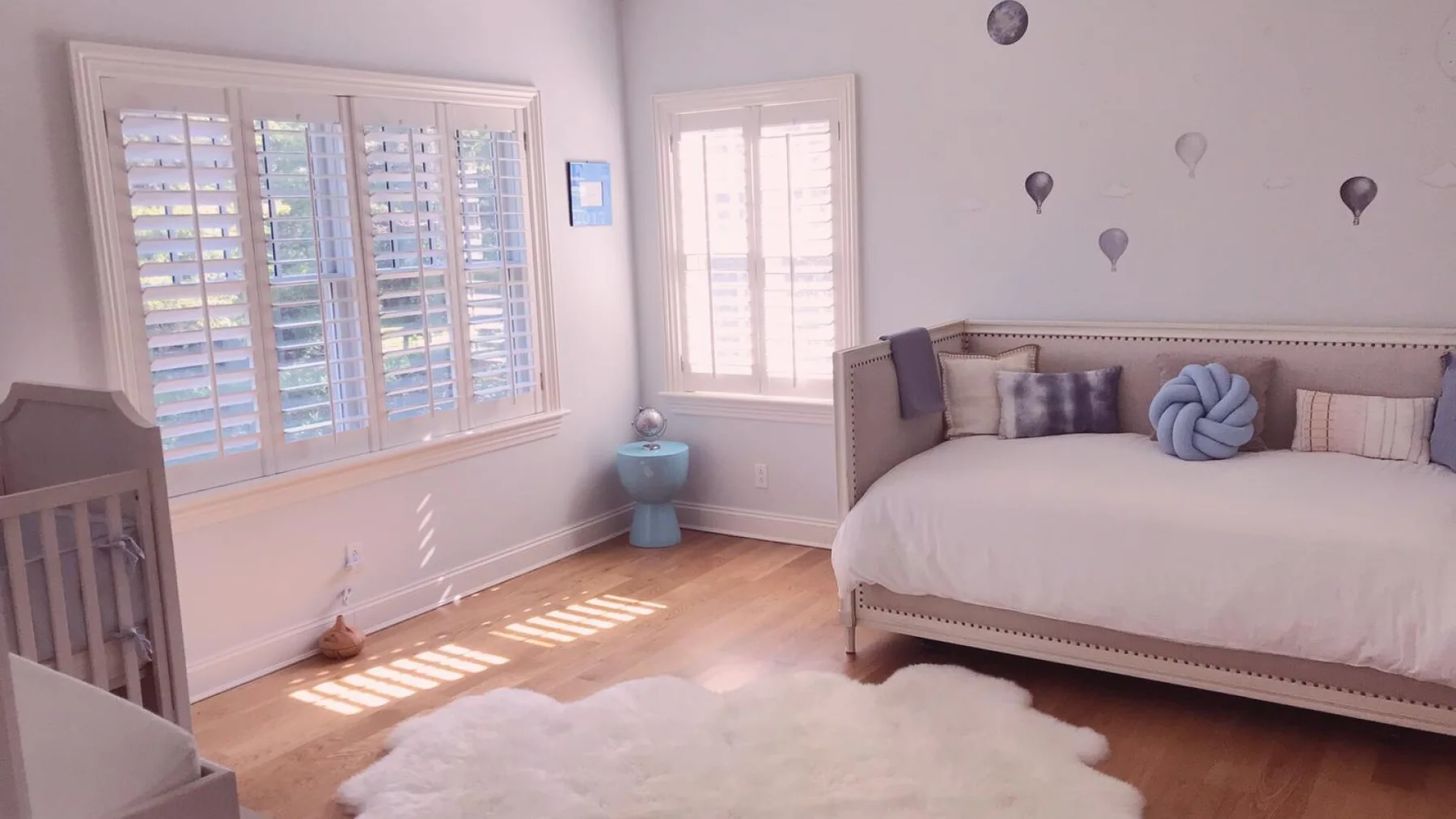 Un dormitorio luminoso con una cama, ventanas con persianas y una alfombra blanca.