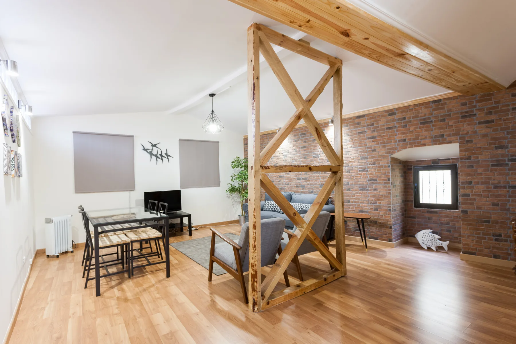 Una luminosa sala de estar y comedor con una pared de ladrillo y vigas de madera expuestas.