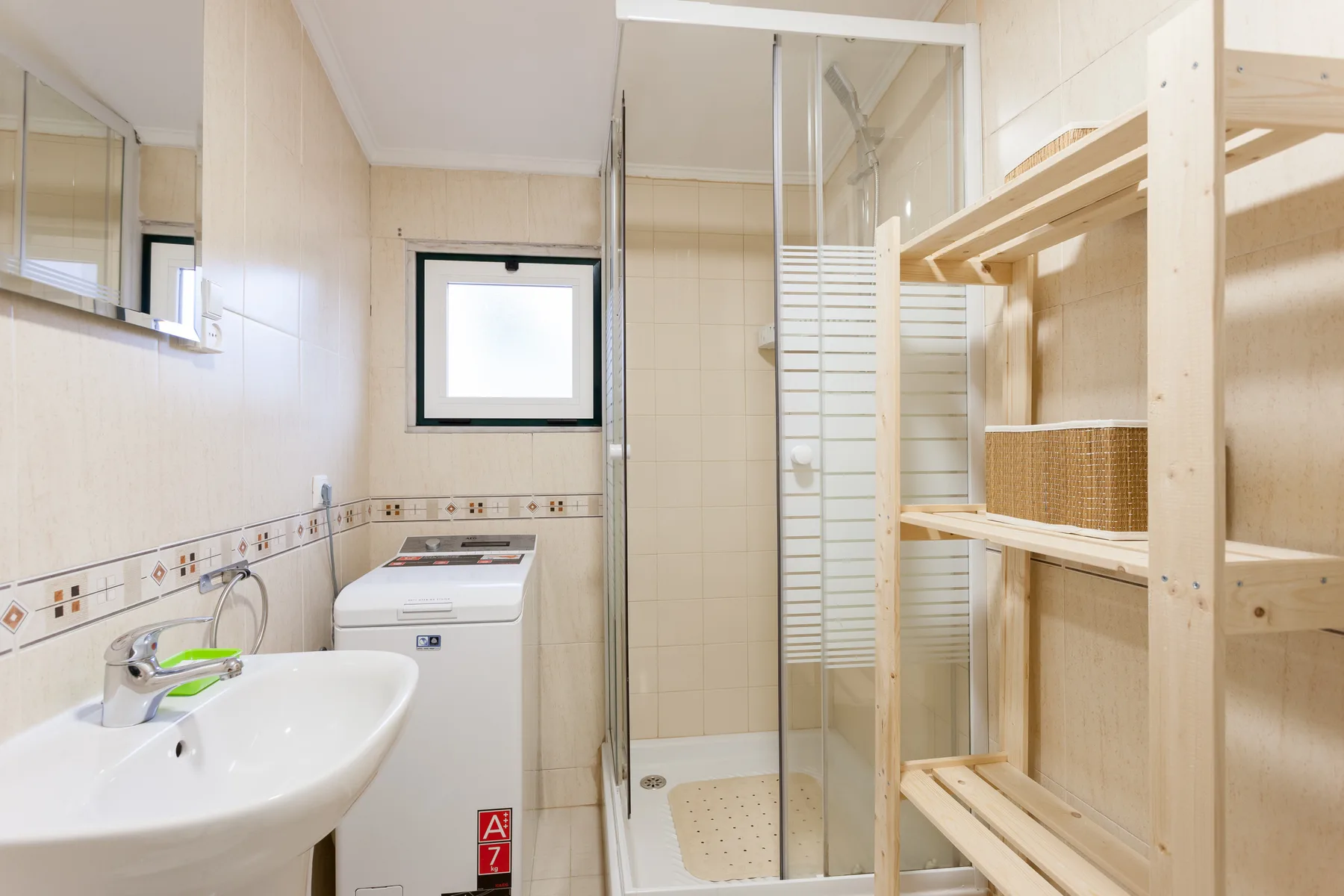 Baño alicatado con lavabo, lavadora y ducha de vidrio.