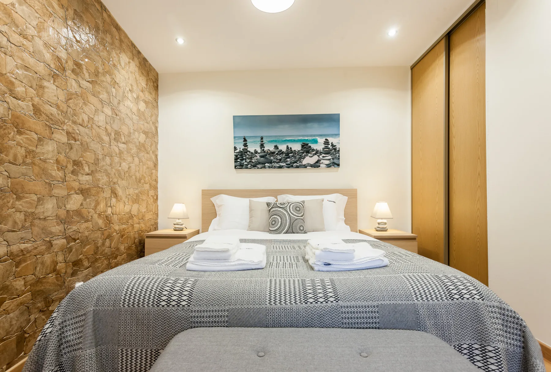 Dormitorio con una cama bien tendida y una pared con textura de piedra.
