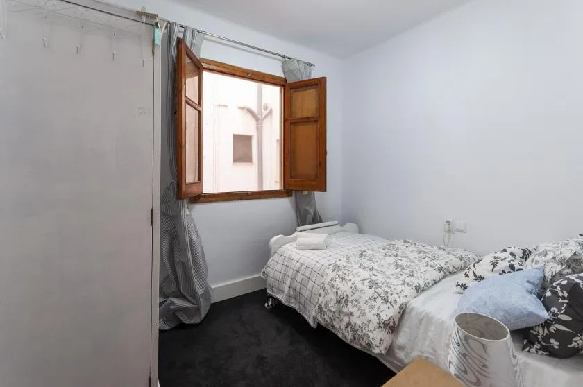 A bedroom with floral bedding and an open wooden window.