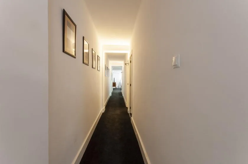 A long hallway with framed pictures along the wall and a dark floor.