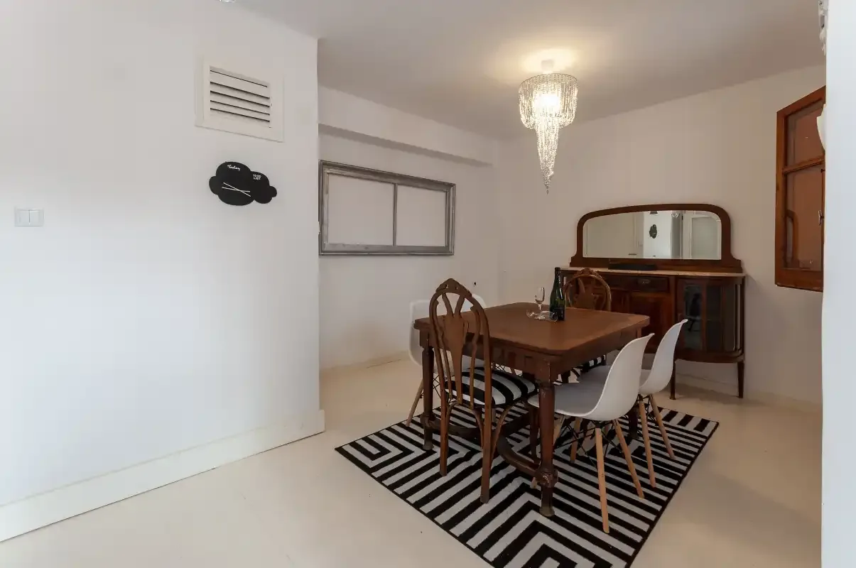 A dining area with a wooden table and chairs on a striped rug.